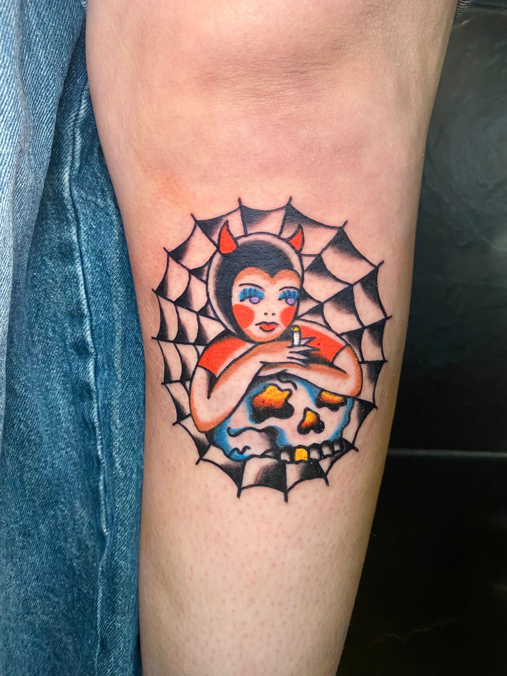 Tatuaje de una mujer diabólica con cuernos rojos, en una telaraña, sosteniendo una calavera.