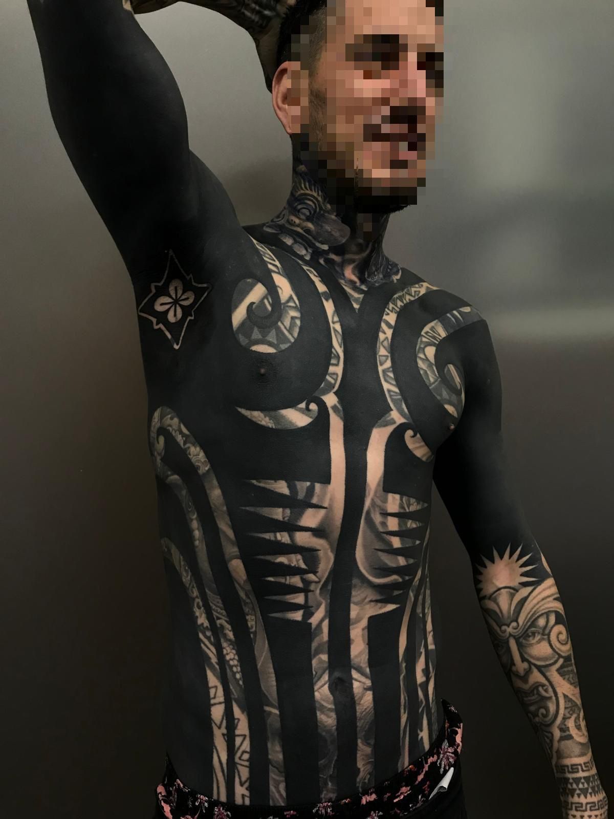 Persona con extensos tatuajes tribales en blanco y negro intrincado que cubren el torso, los brazos y el cuello.