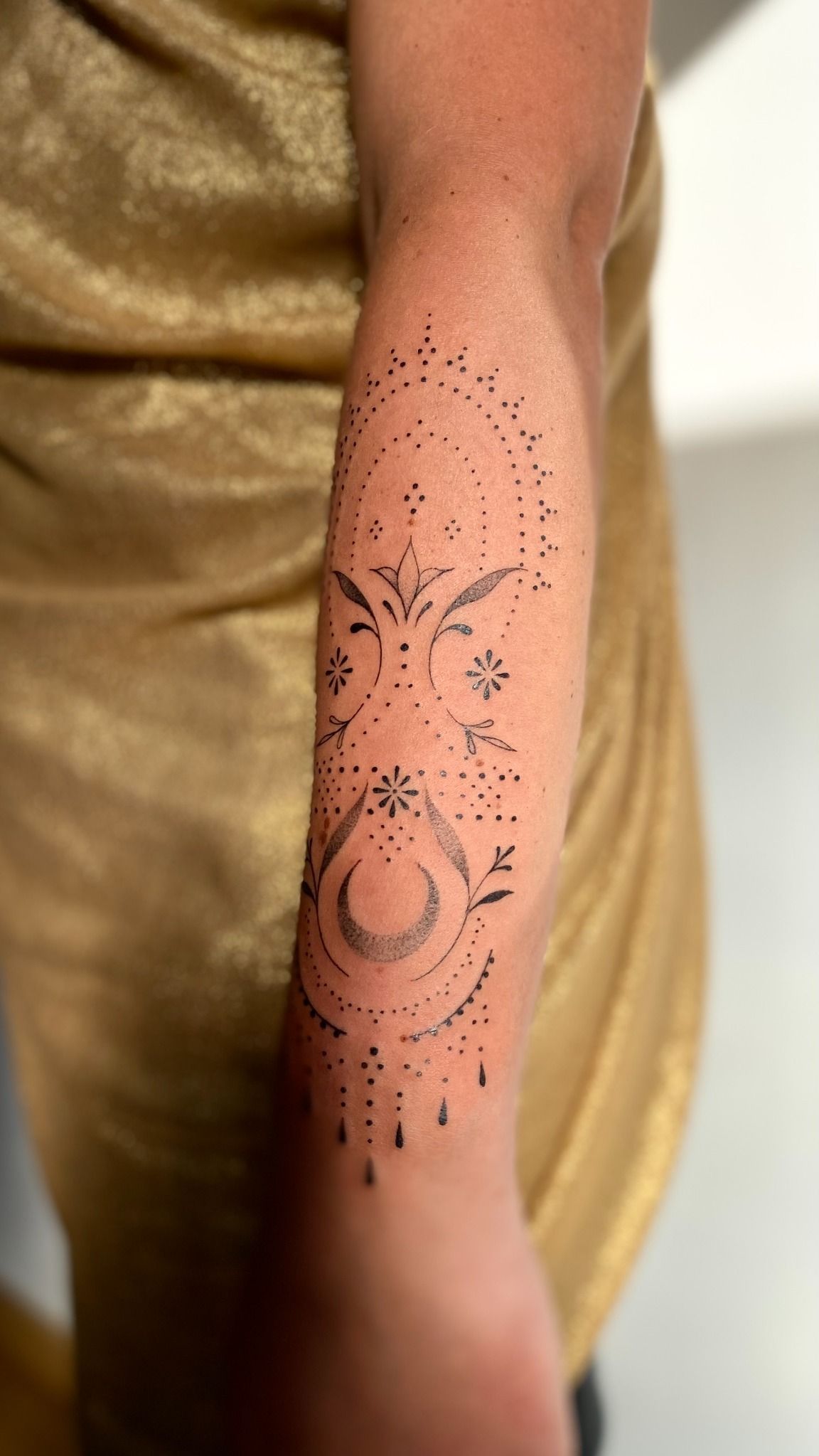 Tatuaje en el brazo, intrincado diseño de puntillismo con luna creciente y elementos florales.