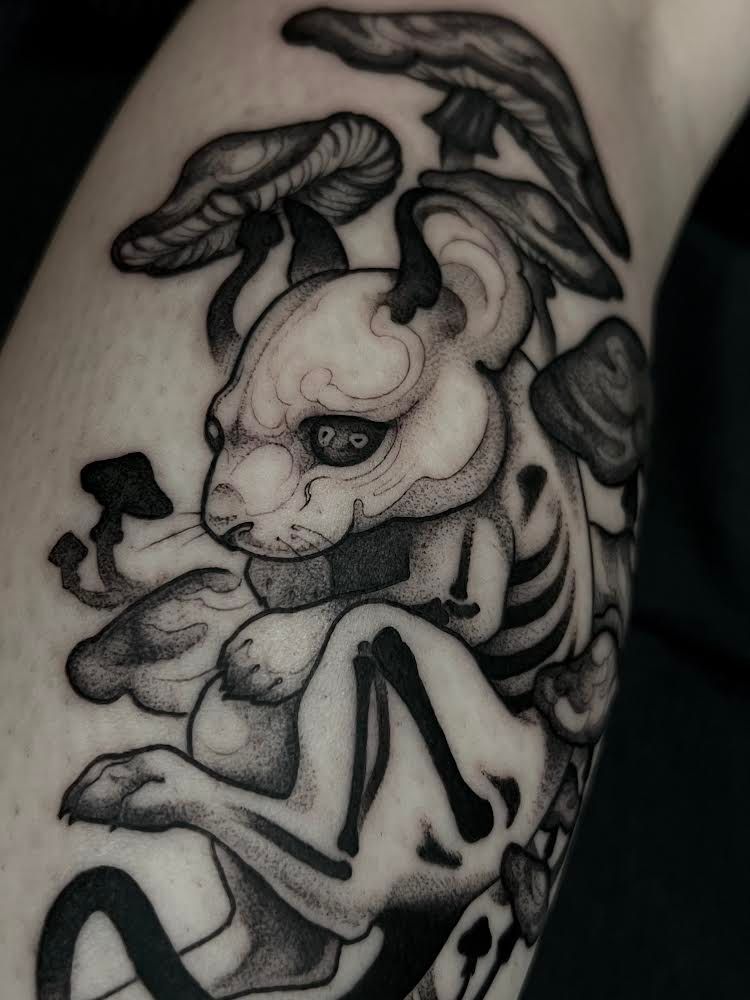 Tatuaje de una criatura parecida a un conejo con esqueleto expuesto, rodeado de hongos, en escala de grises.