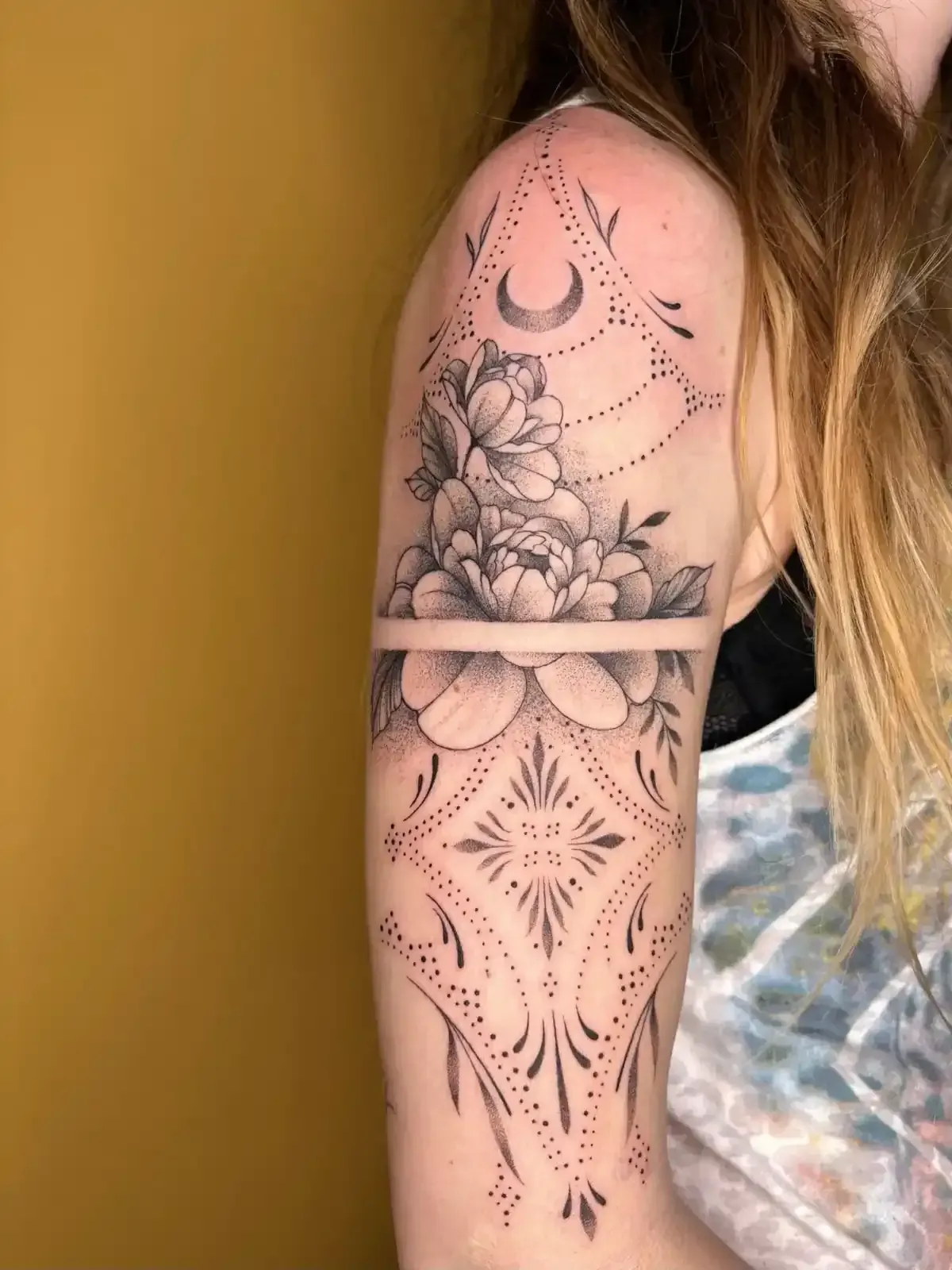 Tatuaje floral y geométrico en la parte superior del brazo de una persona, con peonías.