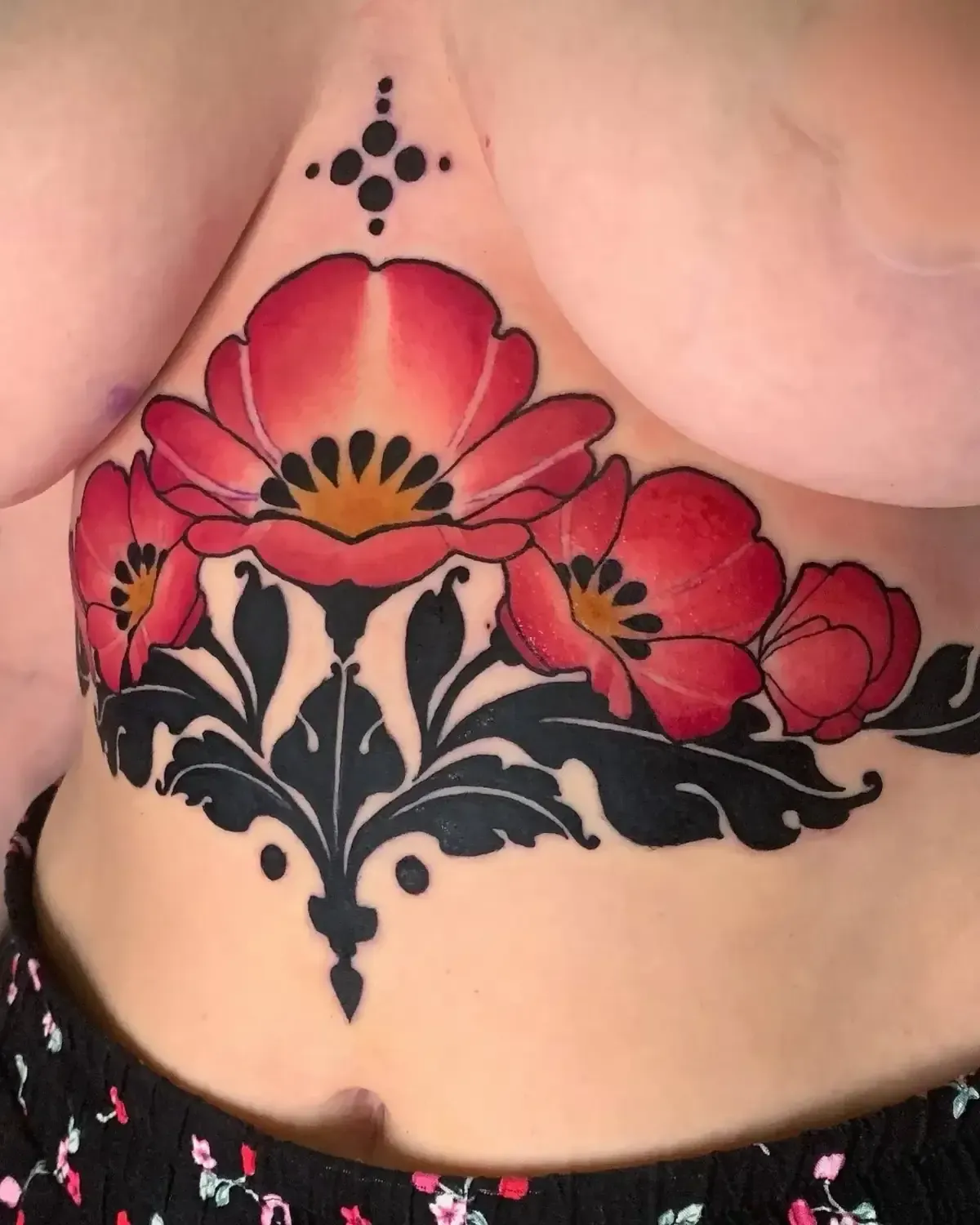 Tatuaje de flores rojas y hojas negras en el torso de una persona.