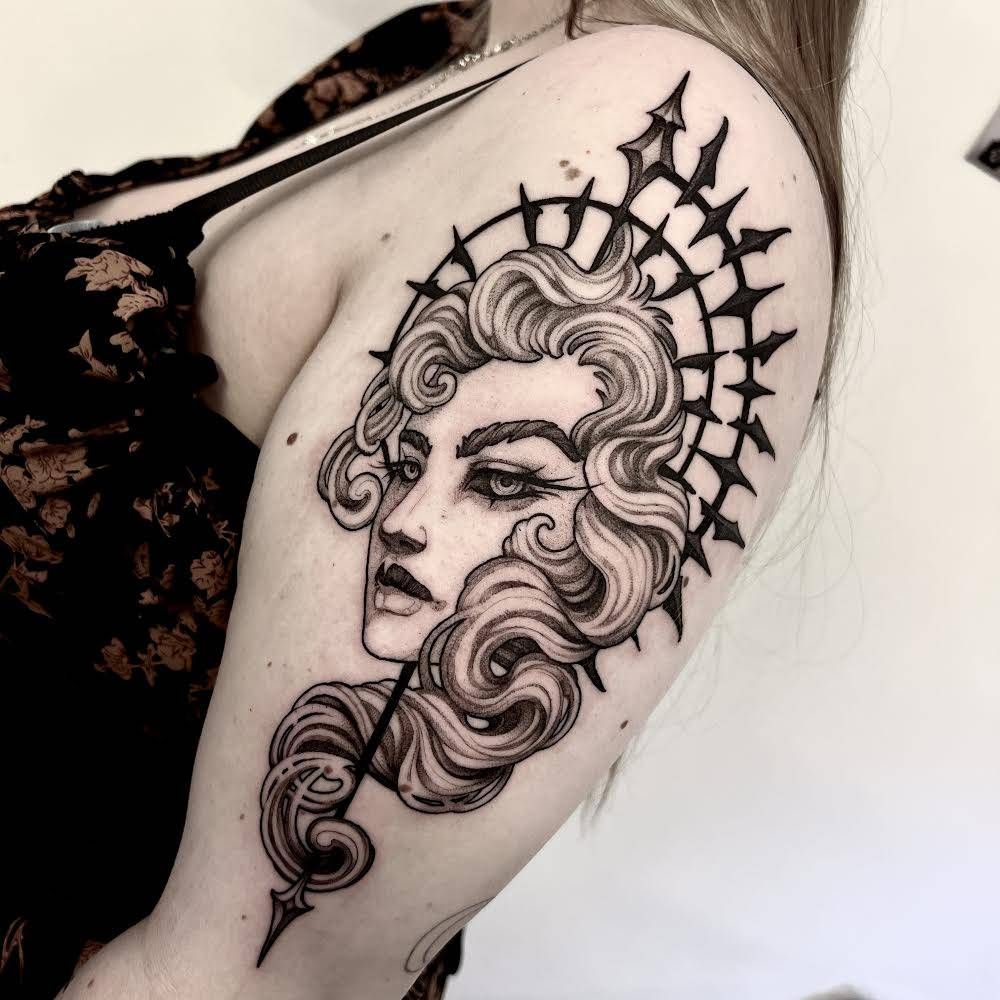 Tatuaje en blanco y negro del rostro de una mujer con un diseño de halo en un brazo.
