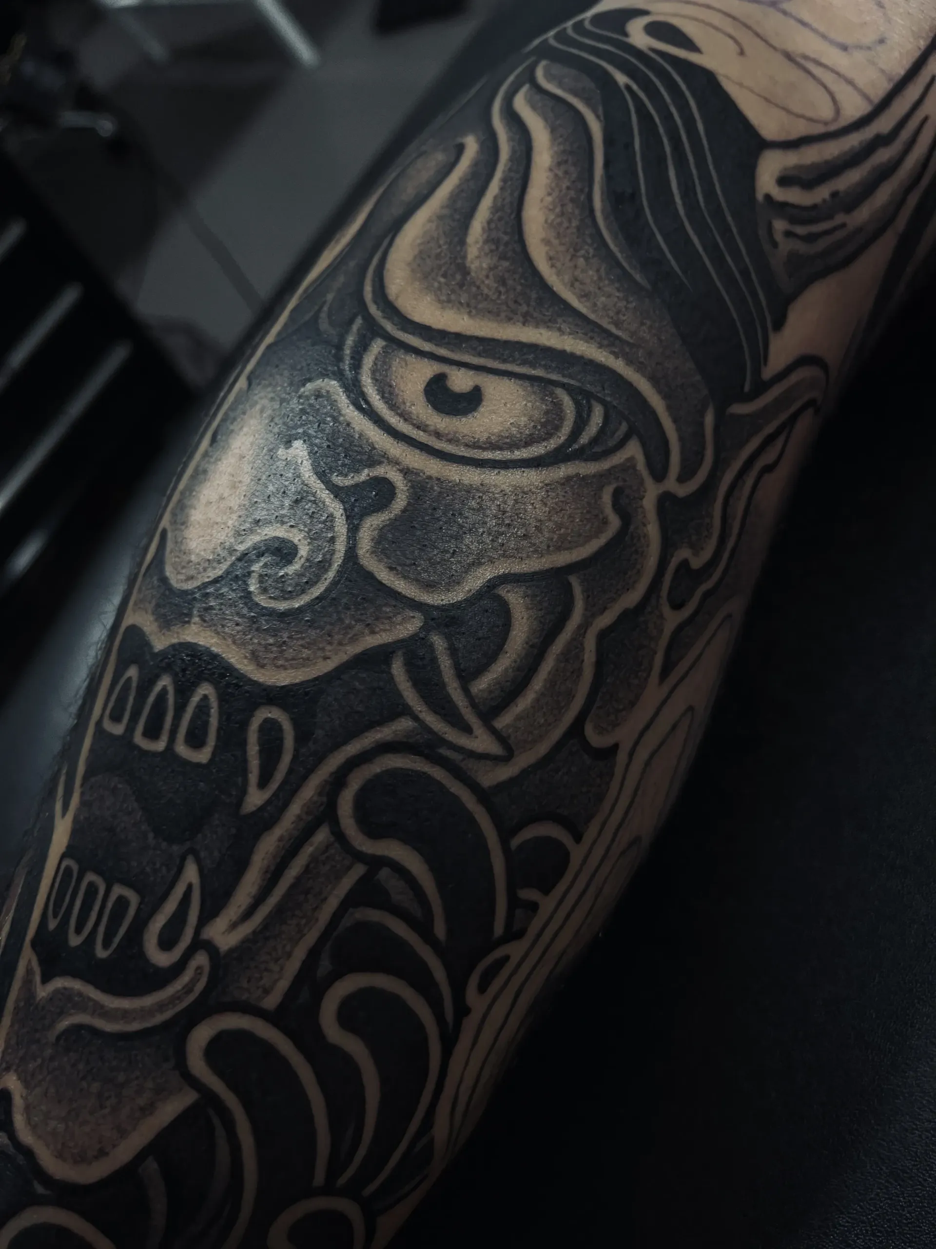 Tatuaje de una máscara de Oni negra y gris con formas similares al agua.