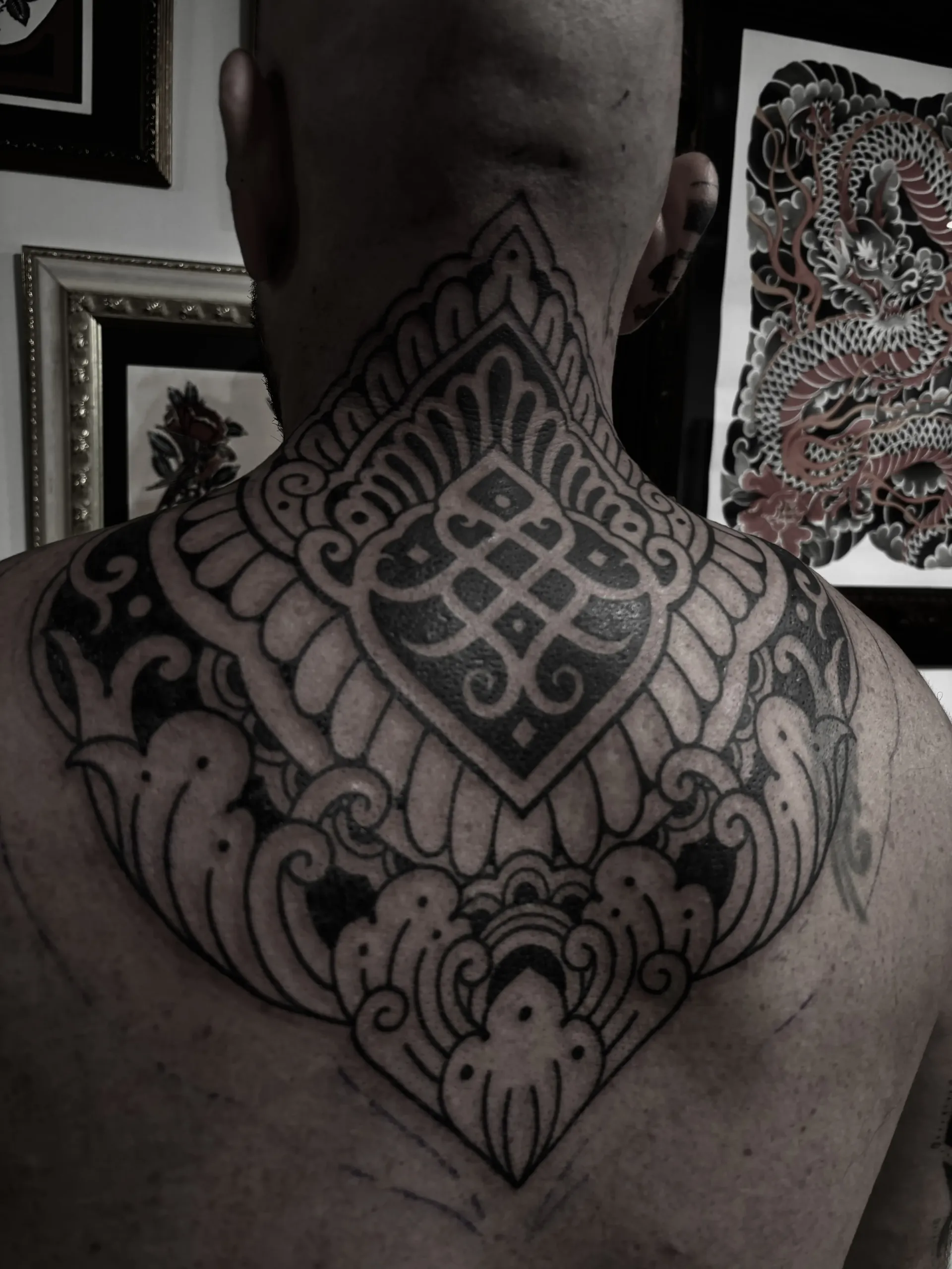 Tatuaje ornamental detallado en el cuello y la parte superior de la espalda de una persona; tinta negra, diseño simétrico.