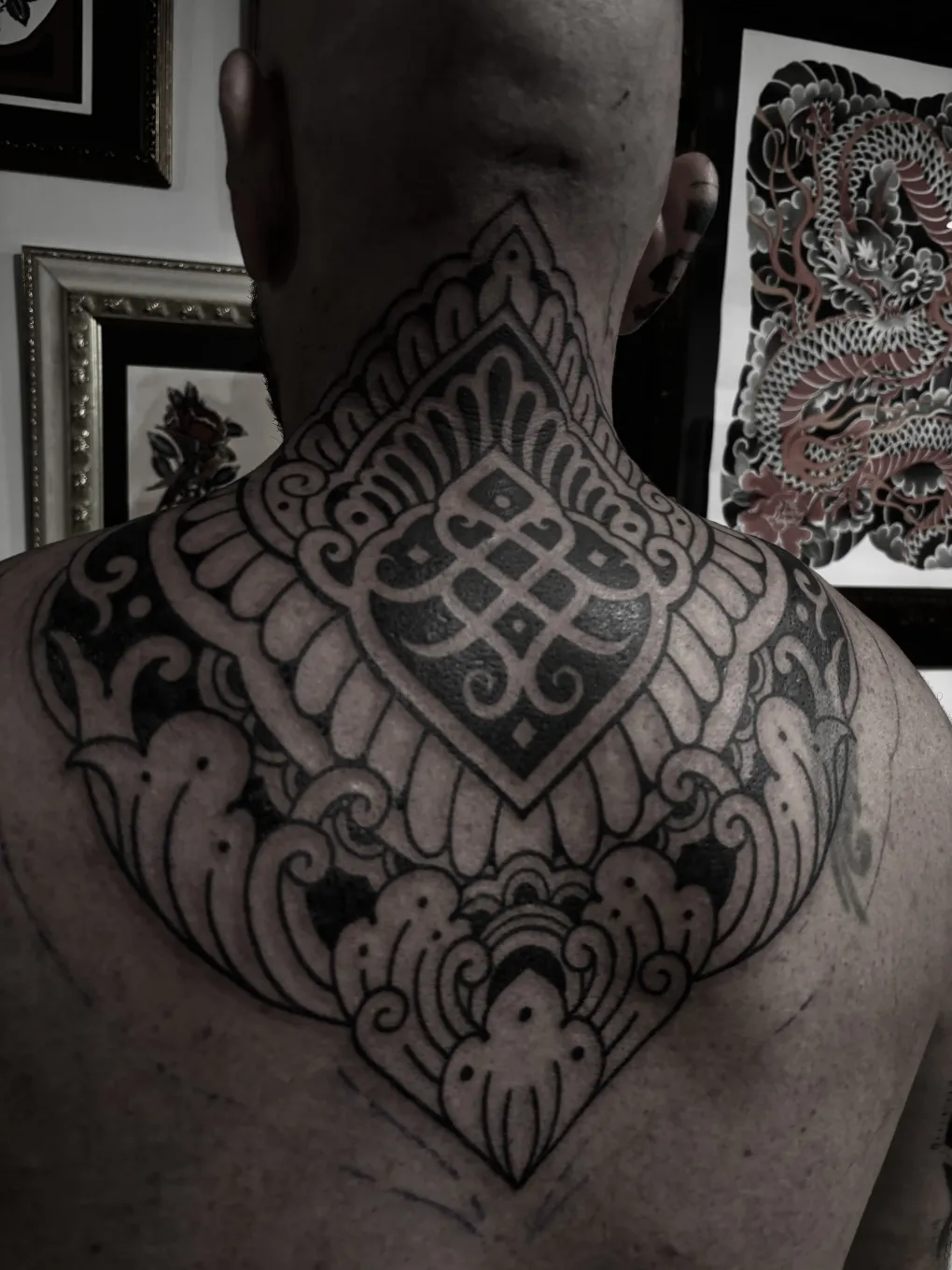Tatuaje en blanco y negro de un diseño ornamentado en el cuello y la parte superior de la espalda de una persona.