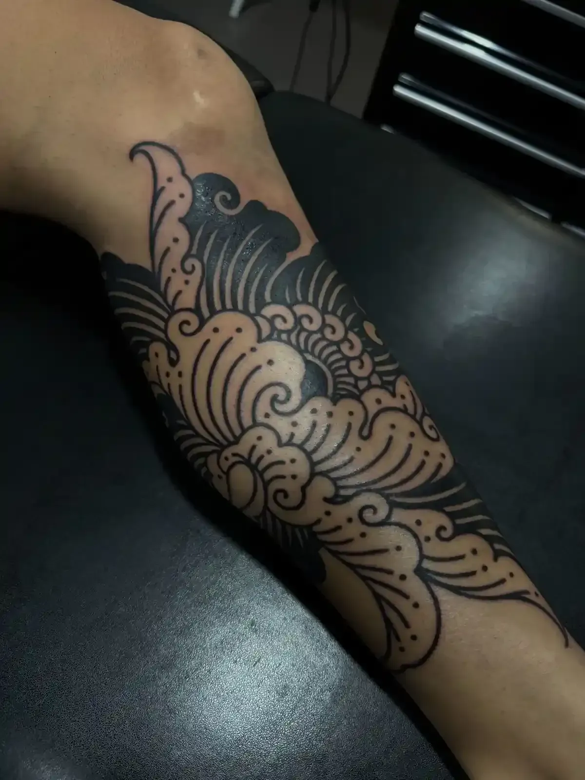 Tatuaje negro de un diseño floral estilizado en el brazo de una persona.