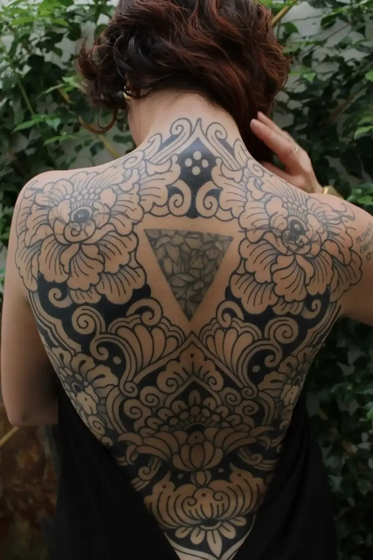 Espalda de mujer con gran tatuaje floral y ornamental negro; triángulo en el centro.