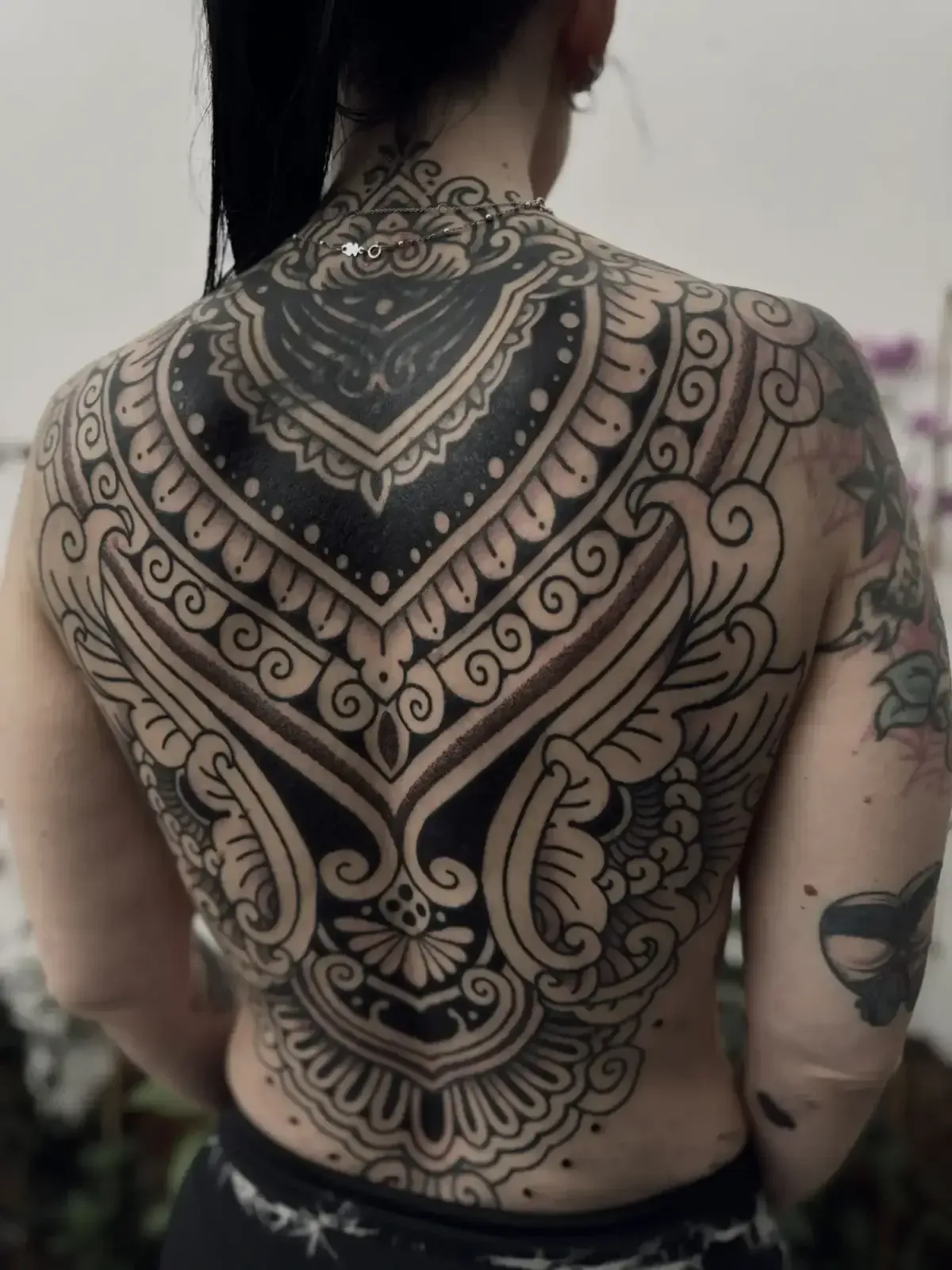 Espalda de mujer cubierta con un intrincado tatuaje ornamental negro.