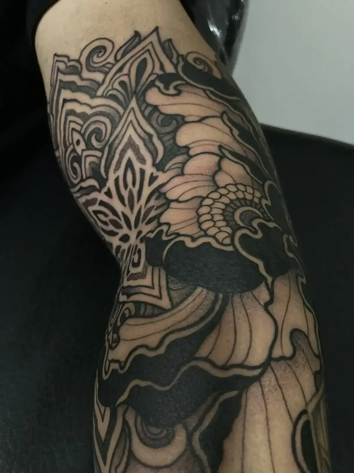 Tatuaje negro y gris en un brazo, con diseños geométricos y florales.