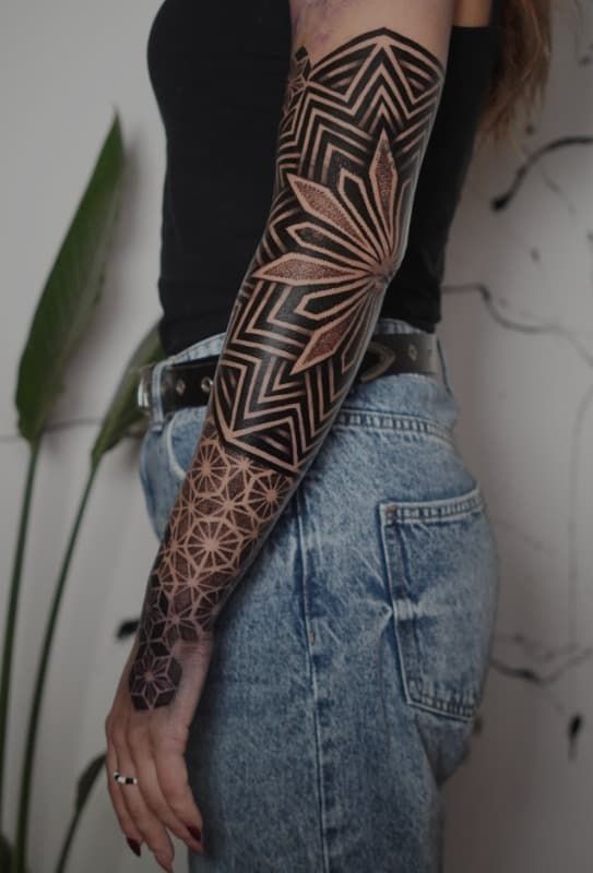 Brazo cubierto de un tatuaje geométrico de henna negra junto a unos vaqueros azules.