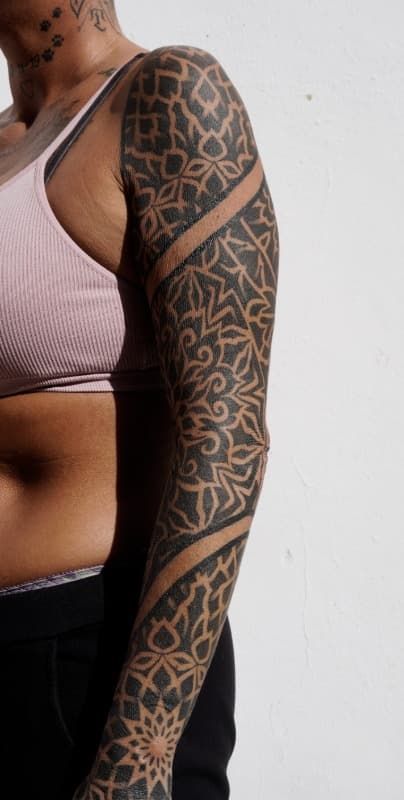 Tatuaje en el brazo con patrones geométricos negros y contornos naranjas en el brazo y el hombro de una persona.