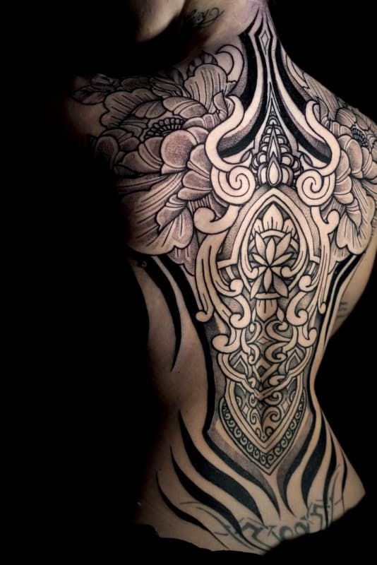 Intrincado tatuaje ornamental en blanco y negro que cubre la espalda y los hombros de una persona.