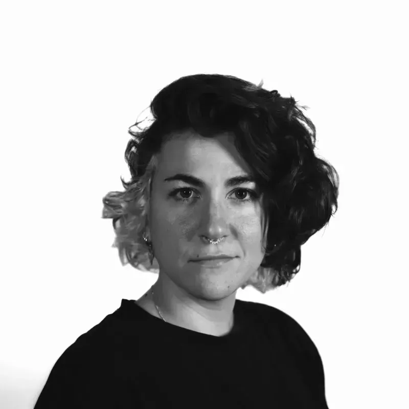 Persona con cabello oscuro, anillo en la nariz y camisa negra mirando directamente a la cámara.