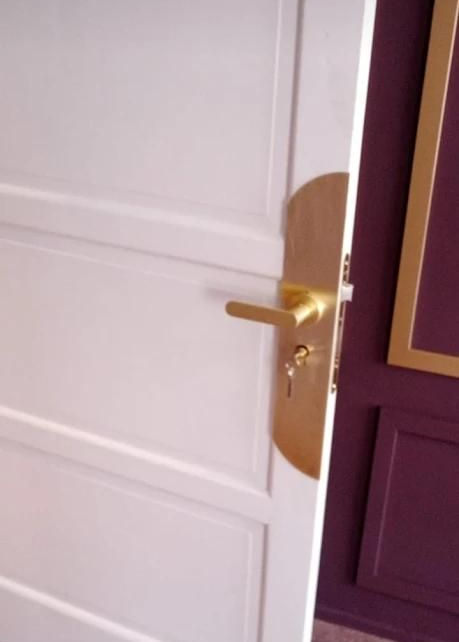 Puerta blanca entreabierta que revela una pared violeta, una manija de puerta y una llave doradas.