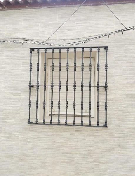 Ventana con rejas decorativas de metal negro sobre una pared de estuco claro.