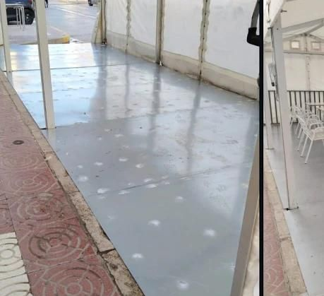 Camino pavimentado bajo una carpa blanca, con gotas de agua en la superficie. Acera de ladrillo a la izquierda.