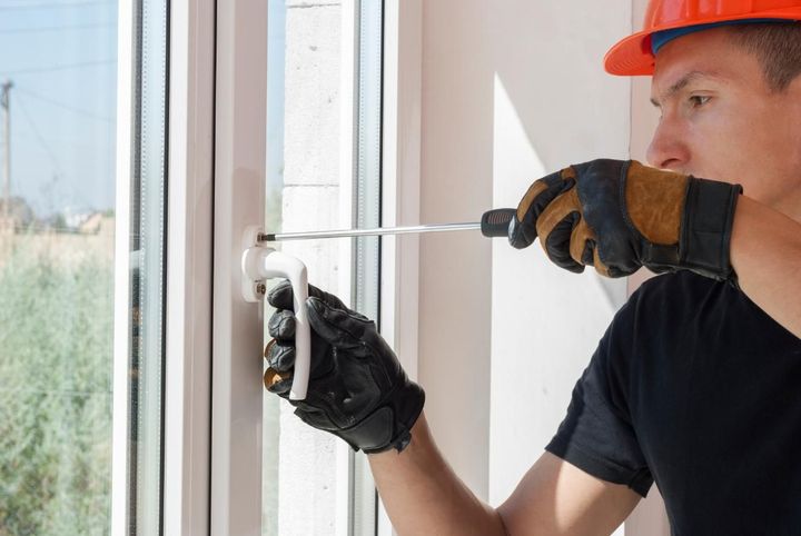 Persona con casco naranja y guantes usando un destornillador para fijar la manija de una ventana.