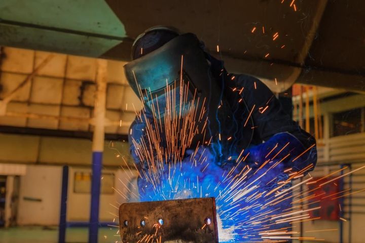 Soldador con equipo de protección azul soldando metal, mientras saltan chispas en un taller.