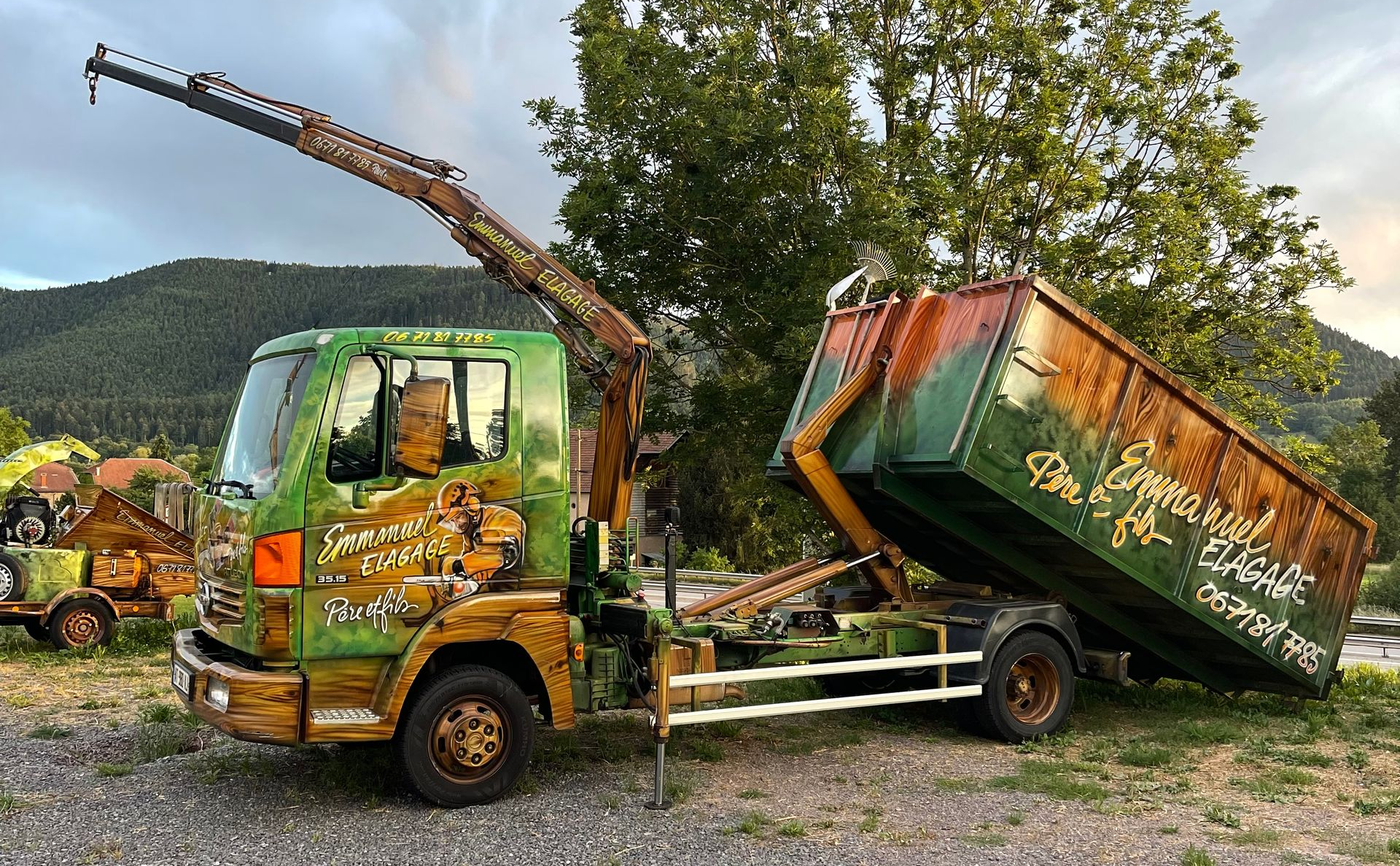 Un camion rouge équipé d'une grue et d'une nacelle remorque une voiture bordeaux sur une rue asphaltée mouillée.