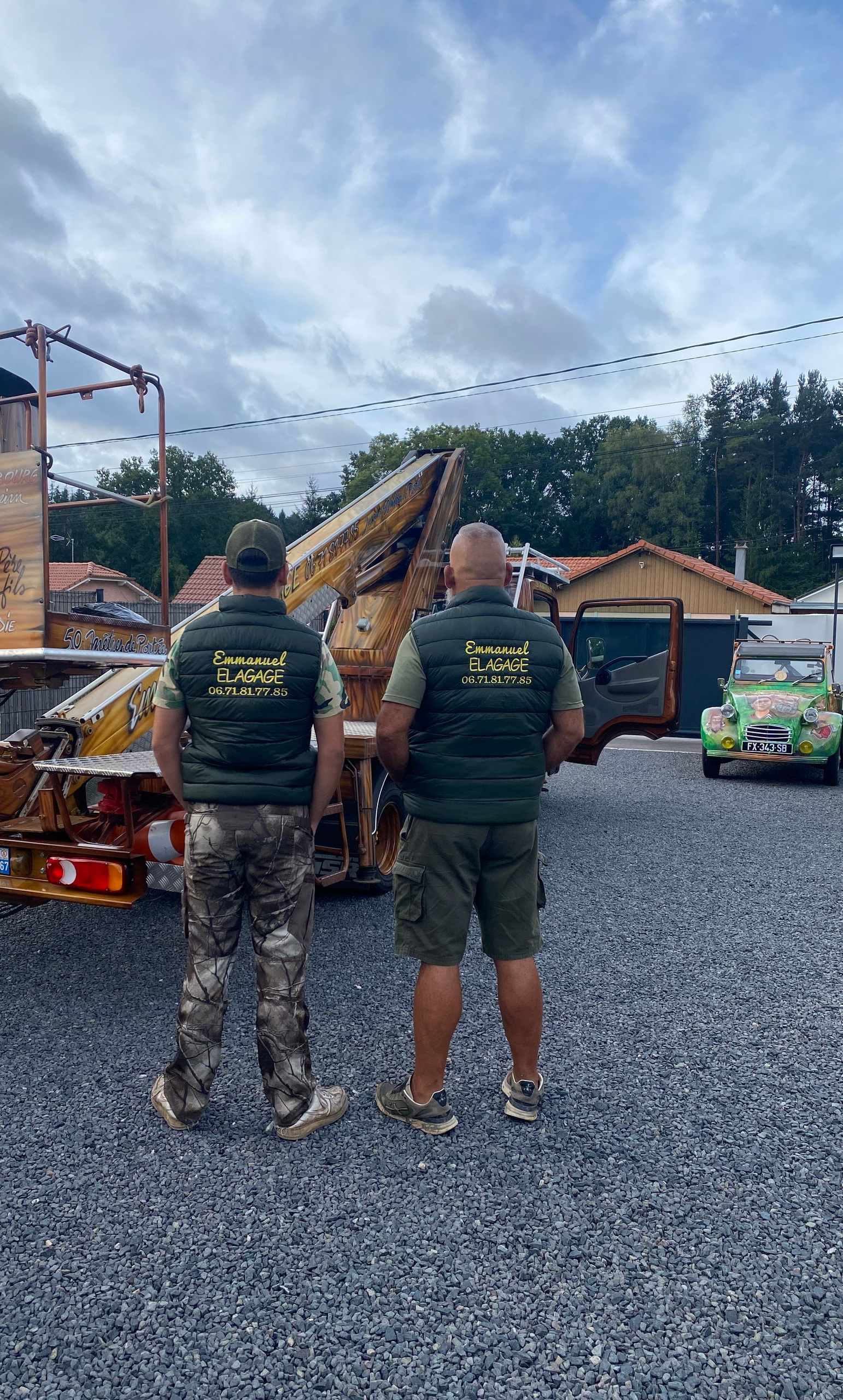Deux hommes portant des gilets se tiennent près d'un camion à l'extérieur. Les gilets comportent des inscriptions au dos.