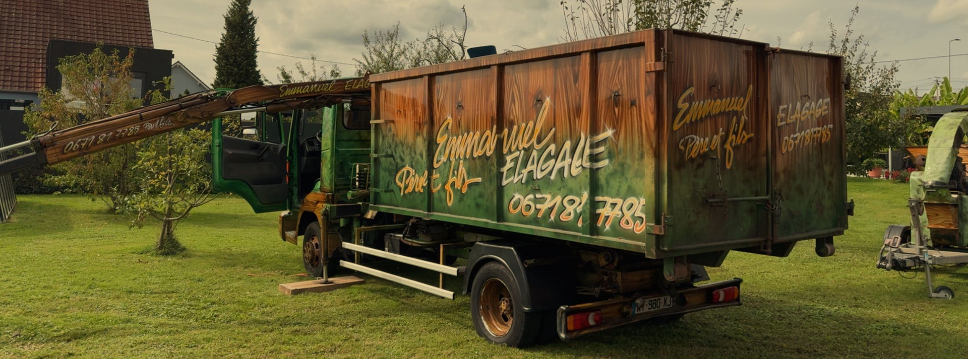 Camion-benne vert rouillé sur l'herbe, couvert de graffitis. Arbres en arrière-plan.