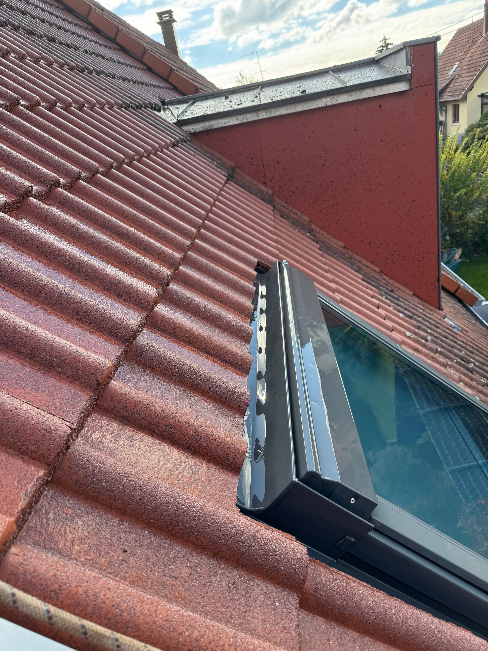Toit en tuiles rouges avec un puits de lumière et une cheminée en briques rouges.