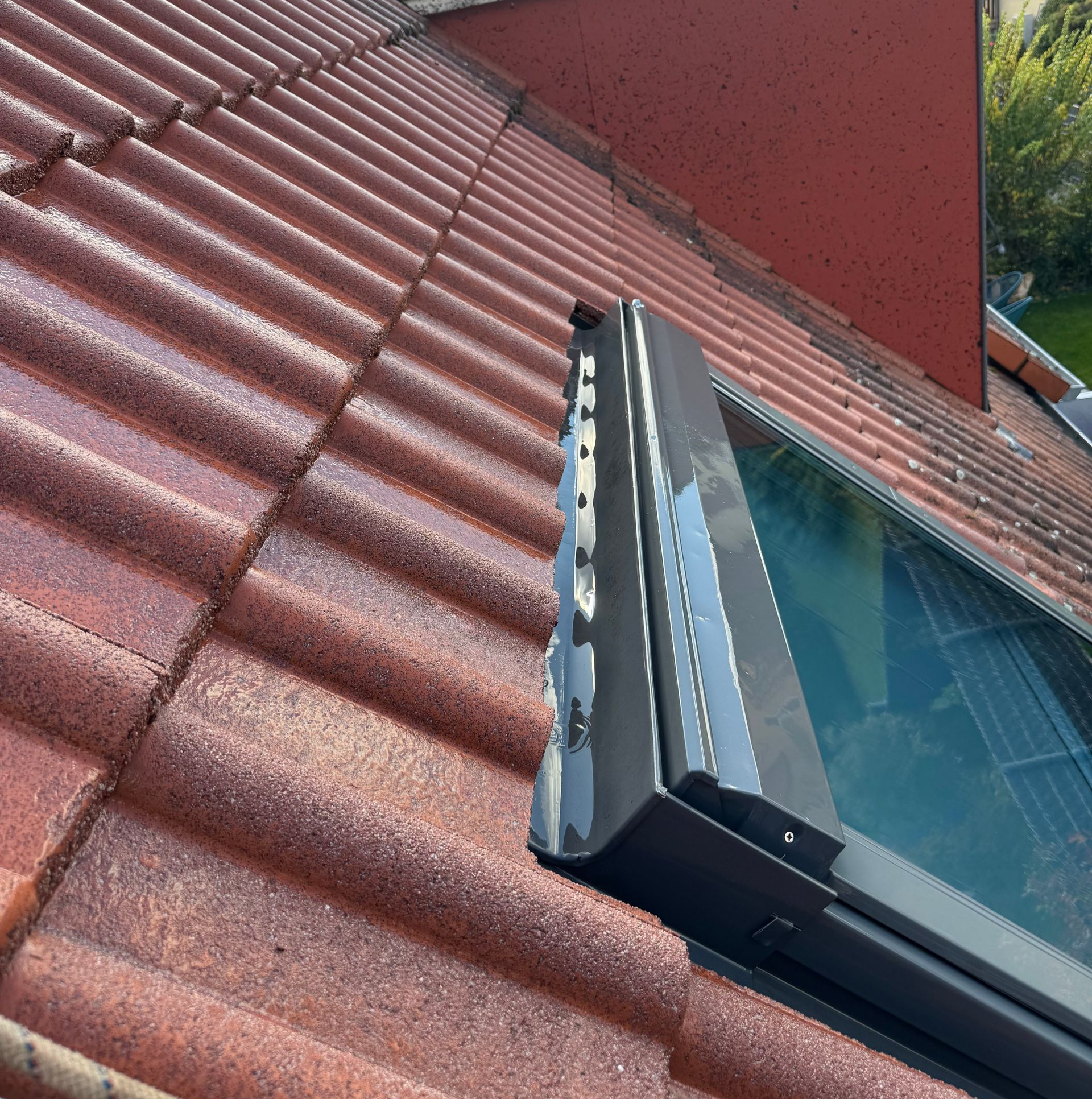 Toit de tuiles rouges avec puits de lumière, cheminée et ciel couvert.