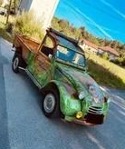 Camionnette vintage verte et marron sur une route ; décor montagneux, ciel bleu.