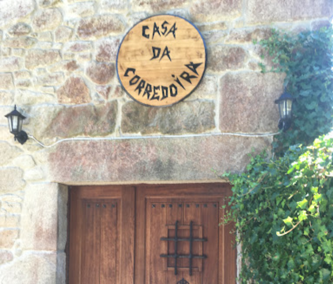 Letrero "Casa da Corredoura" sobre puertas de madera en un edificio de piedra, con hiedra creciendo en el costado.