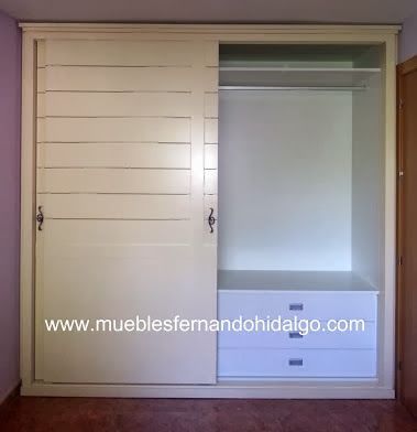 Un armario blanco con puertas correderas y cajones en un dormitorio.