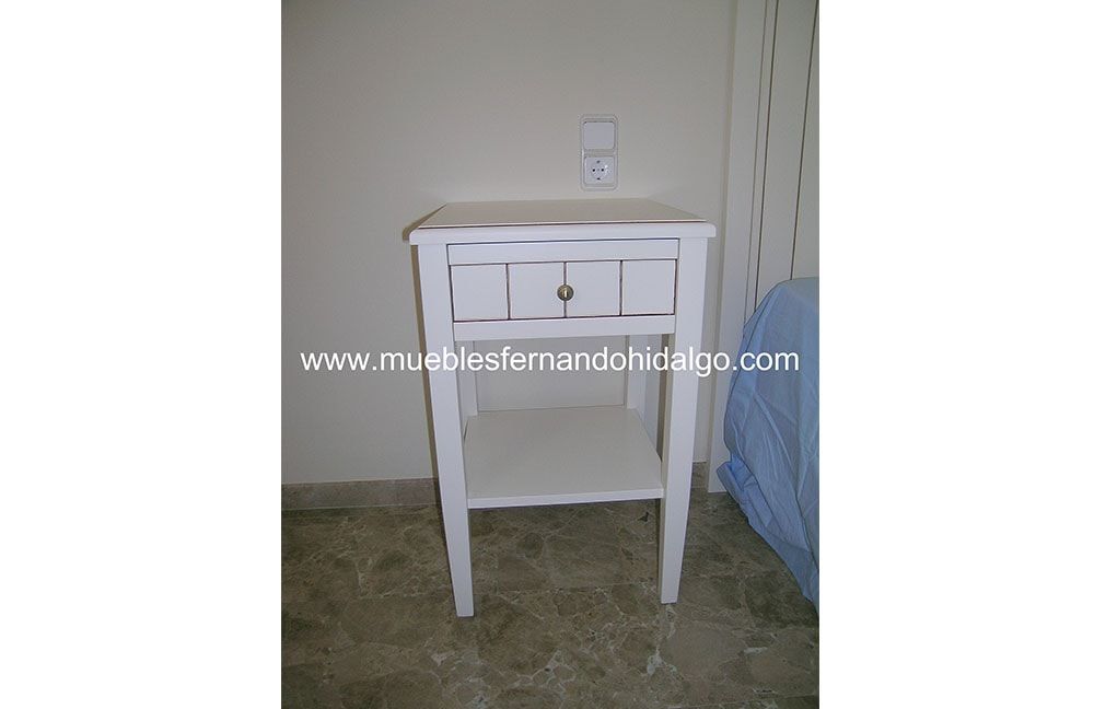 Una pequeña mesita de noche blanca con un cajón y un estante.