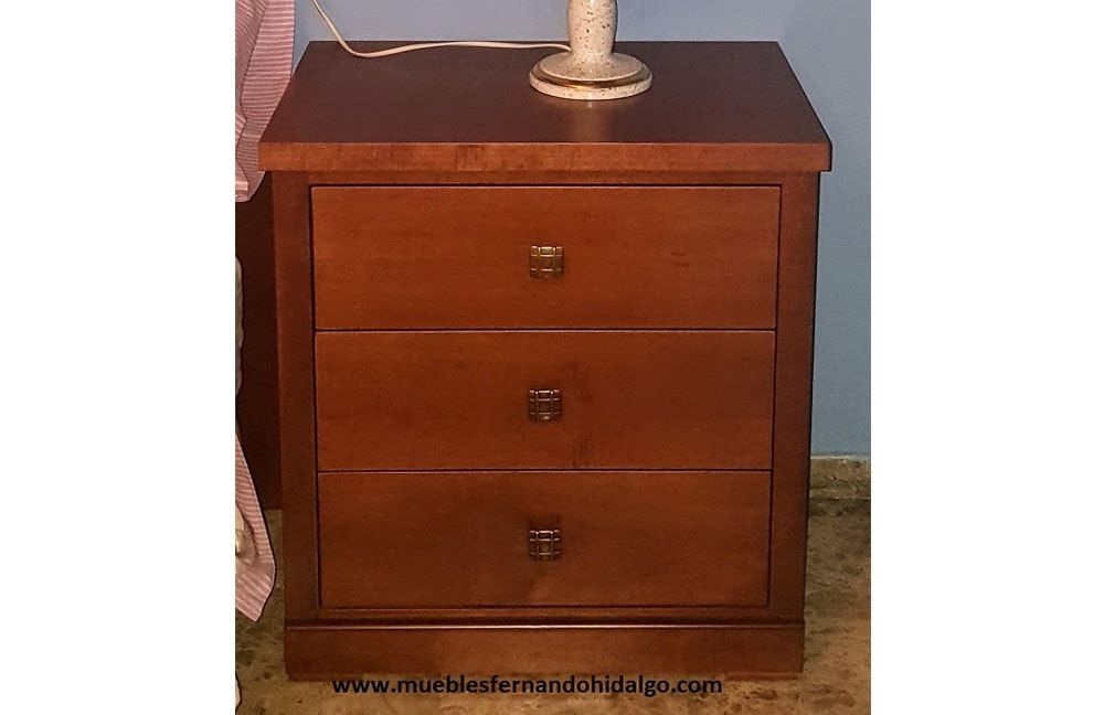 Una mesita de noche de madera con tres cajones y una lámpara encima.