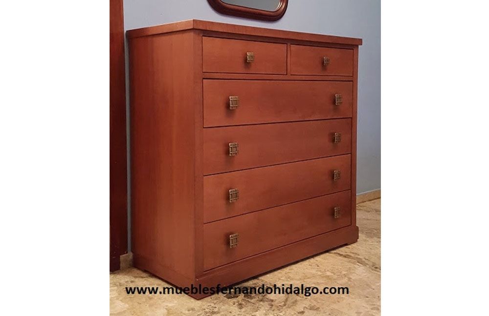 En una habitación hay una cómoda de madera al lado de un espejo.