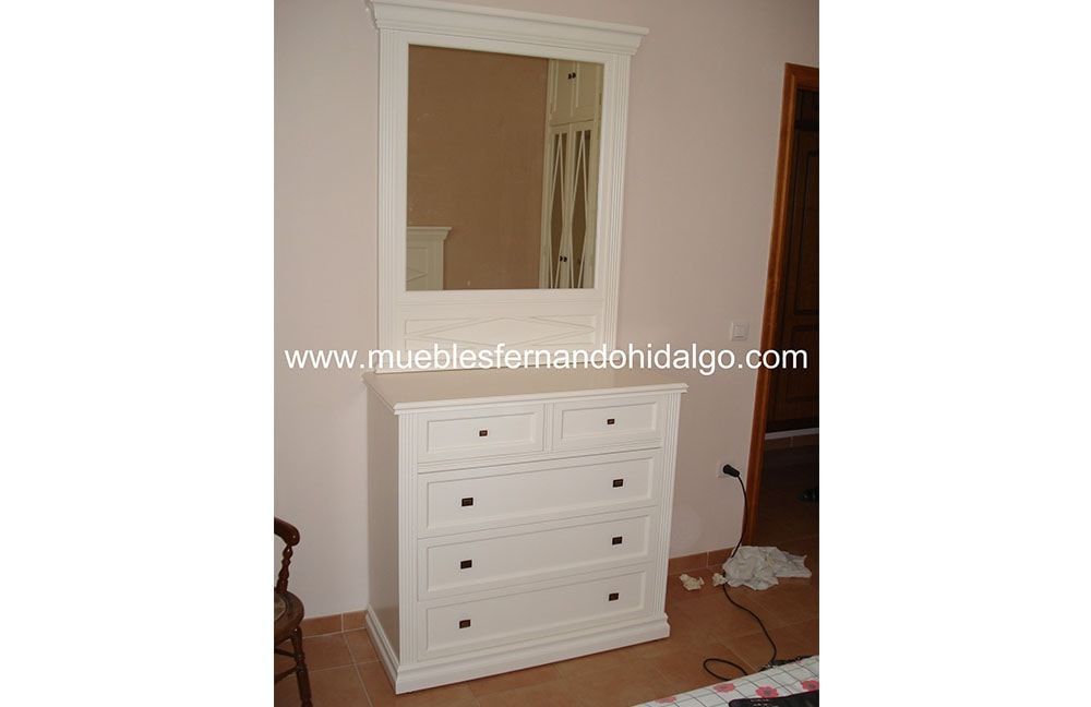 Una cómoda blanca con cajones y un espejo en un dormitorio.