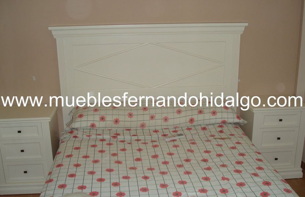 Una cama con cabecero blanco y mesitas de noche con la web www.mueblesfernandohidalgo.com en la parte inferior
