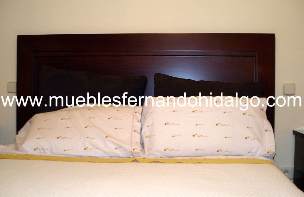 Una cama con dos almohadas y un cabecero de madera con la web www.mueblesfernandohidalgo.com al pie