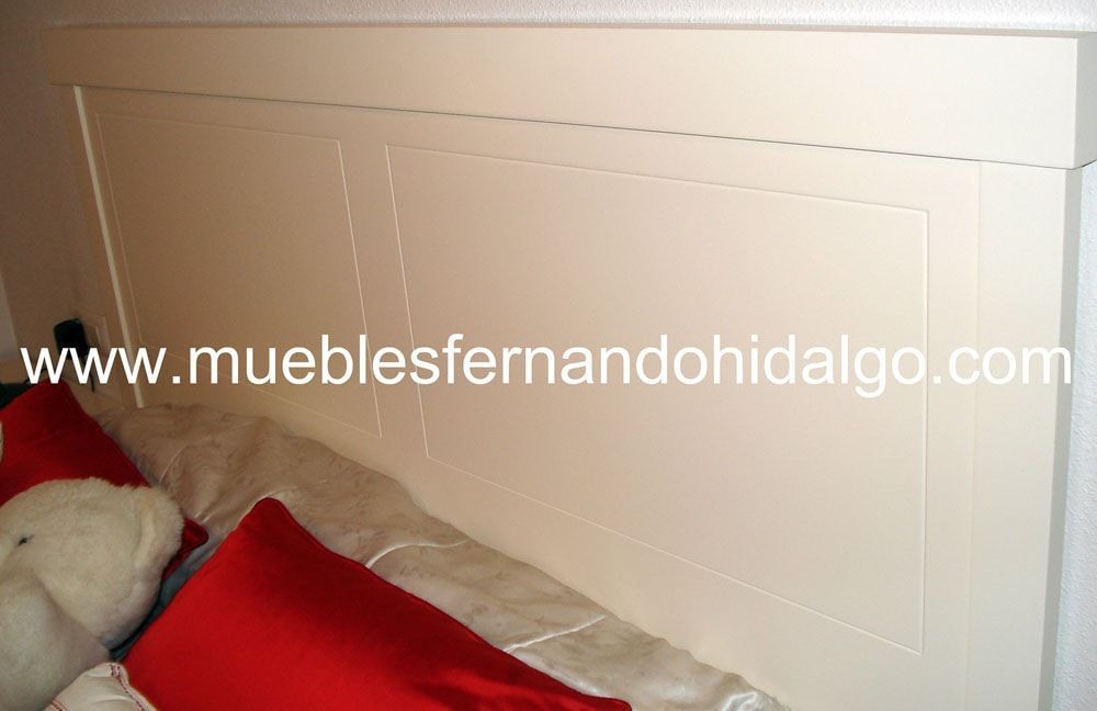 Una cama con almohadas rojas y un cabecero blanco que dice www.mueblesfernandohidalgo.com