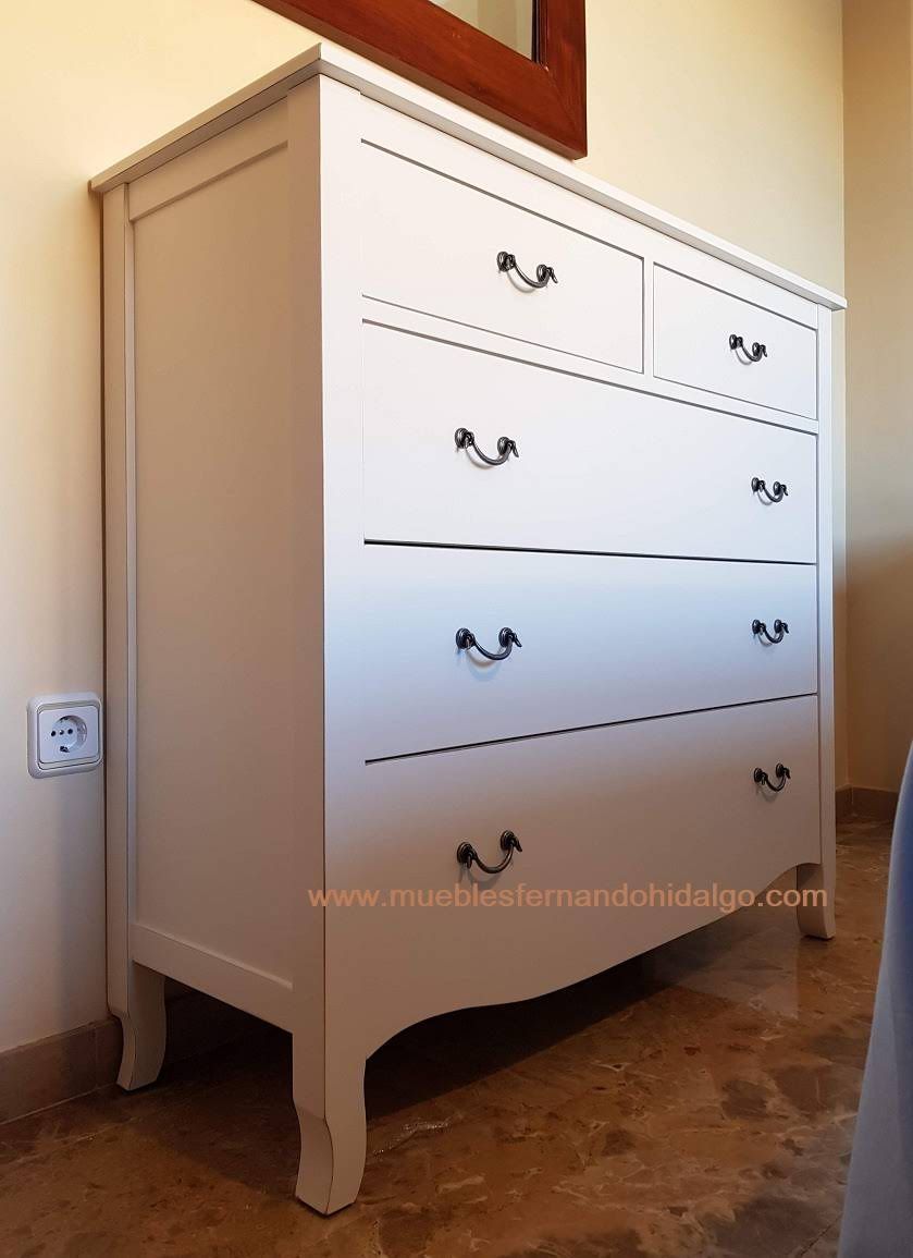 Hay una cómoda blanca en un dormitorio al lado de un espejo.