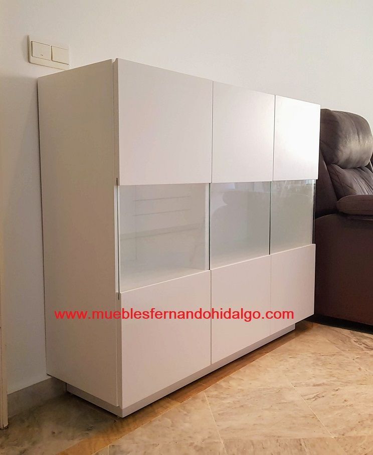 Un armario blanco con puertas de cristal se encuentra en una sala de estar al lado de un sofá.