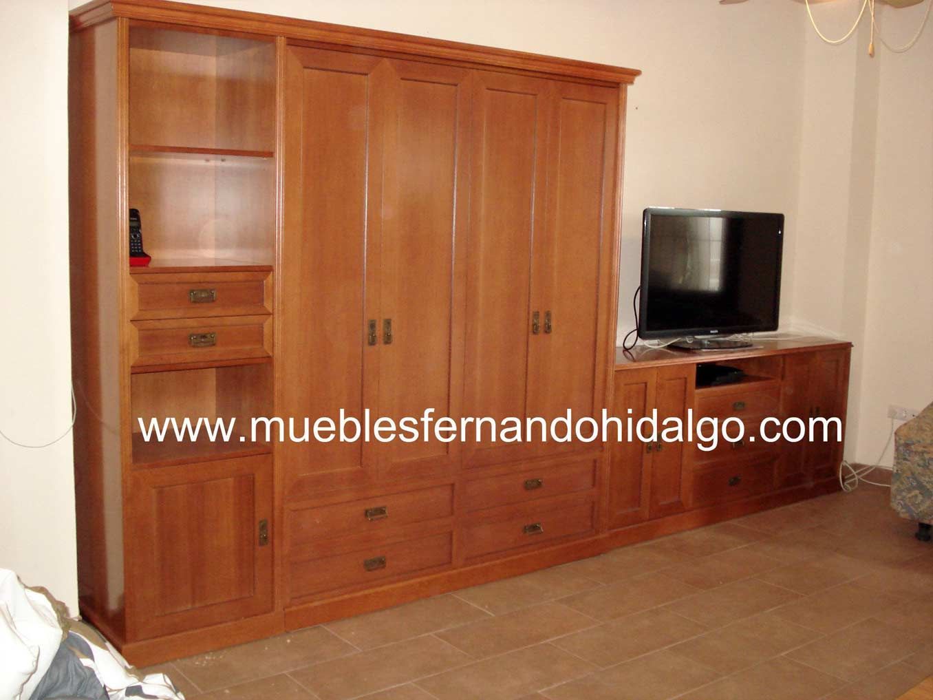 Un salón con un gran armario de madera y una televisión de pantalla plana de www.mueblesfernandohidalgo.com