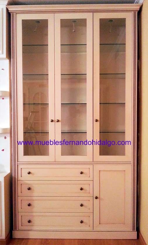 Un mueble blanco con puertas de cristal y cajones tiene en la parte inferior la web www.mueblesfernandohidalgo.com