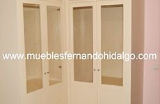Un armario blanco con puertas de cristal en una habitación con una pared rosa.