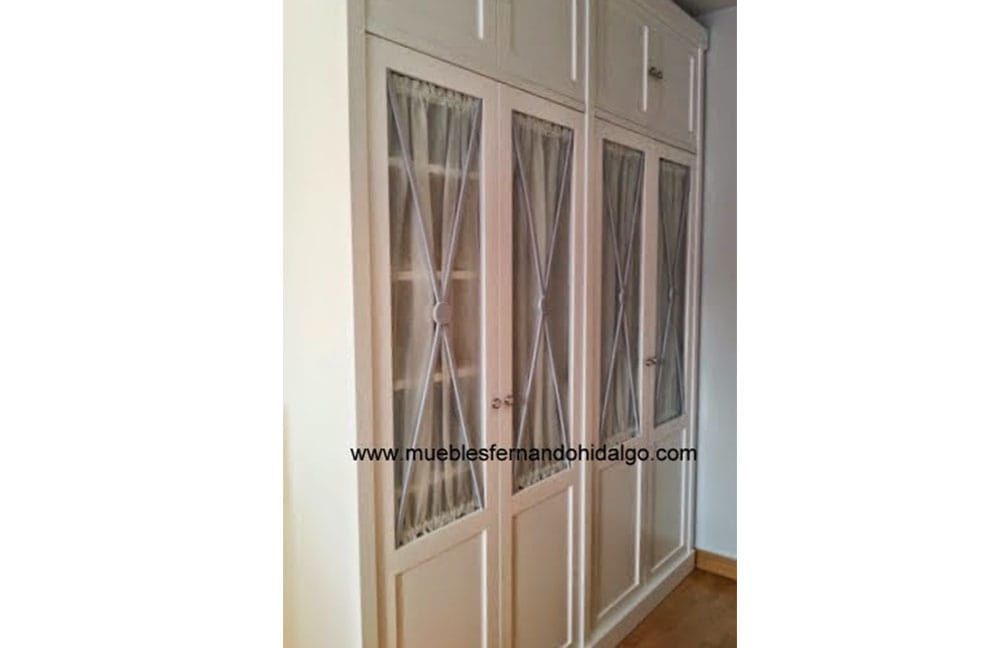 Un armario blanco con puertas de cristal y cortinas en una habitación.