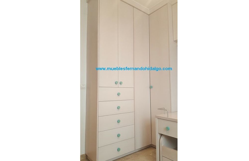 Un rincón de una habitación con armarios y cajones blancos.