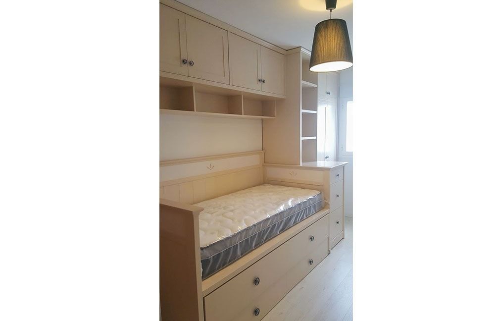 Un dormitorio con una cama, una cómoda, estantes y una lámpara.