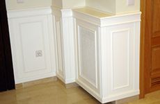 Un rincón de una habitación con paneles blancos y una puerta de madera.