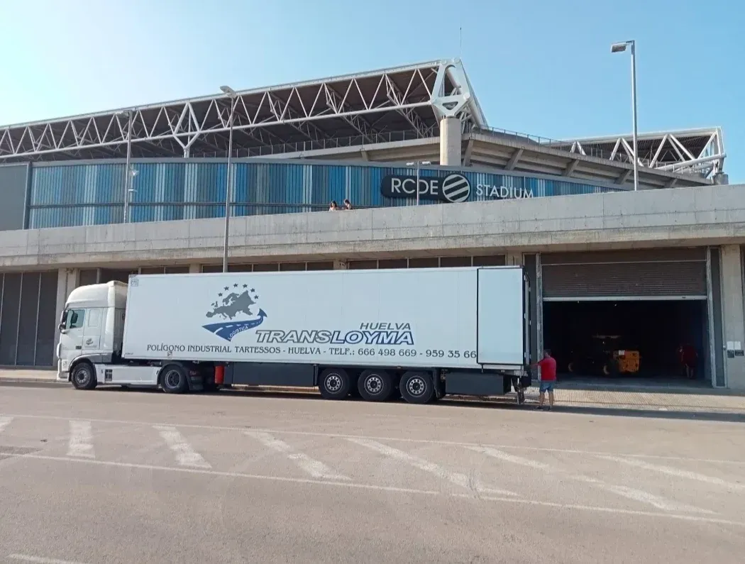 Repartidor cargando cajas en una camioneta blanca afuera de un almacén.