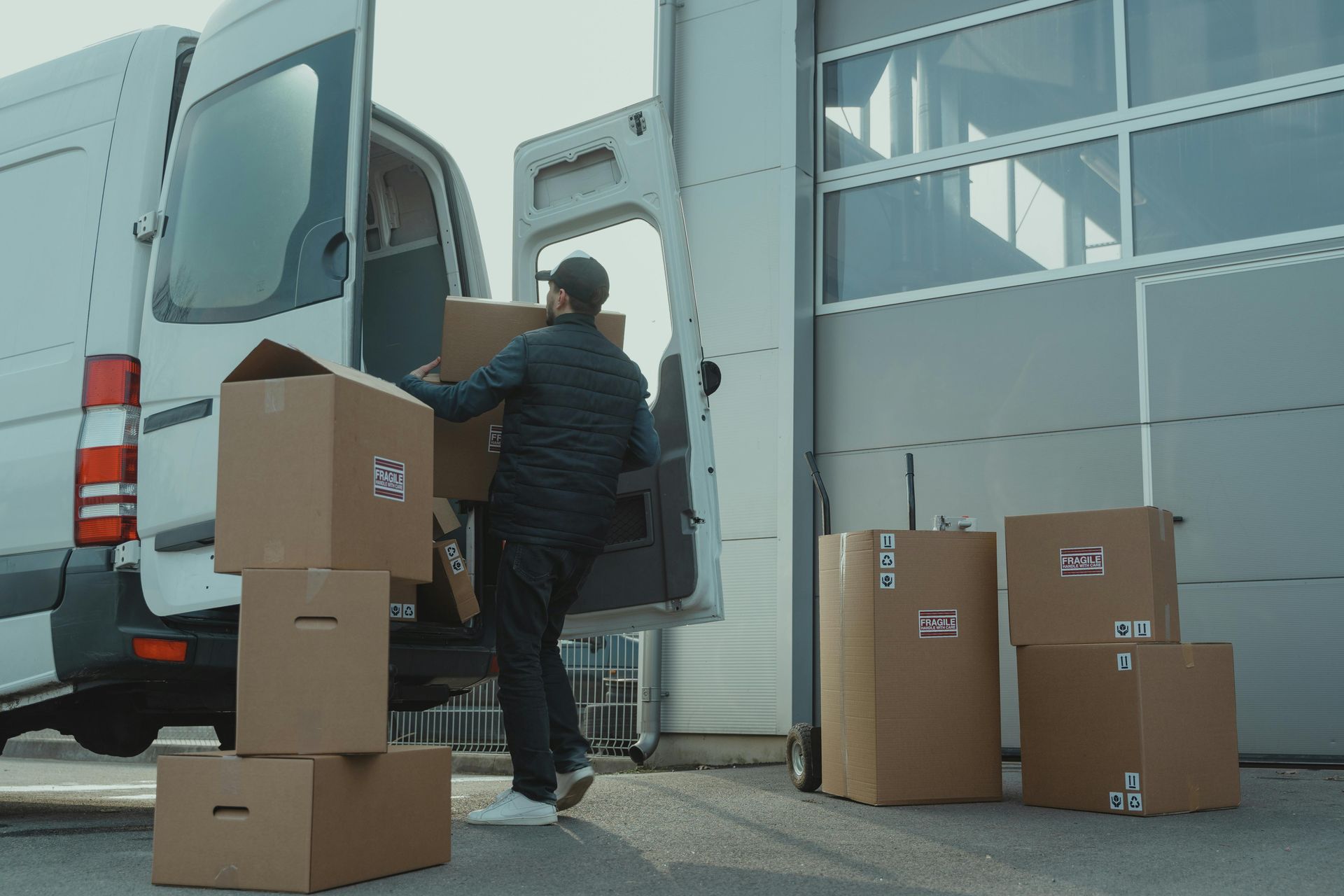 Repartidor cargando cajas en una camioneta blanca afuera de un almacén.