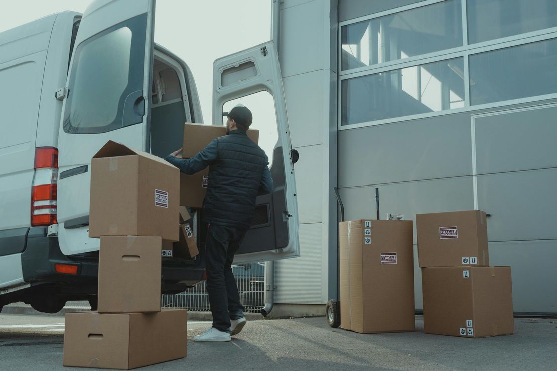Repartidor cargando cajas en una camioneta blanca afuera de un almacén.